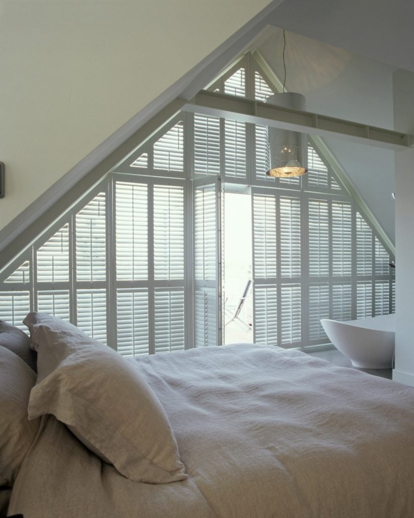 Large floor to ceiling triangular shaped window in bedroom with white shutters - Shutters Norfolk - Norwich Sunblinds