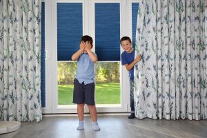 Two boys playing hide and seek with beautiful curtains and perfect fit blinds by Norwich Sunblinds