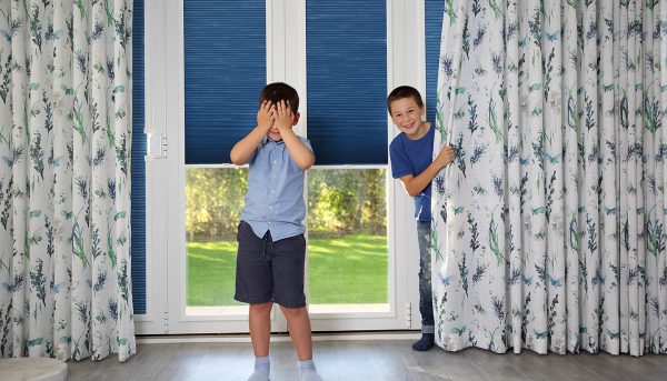 Two boys playing hide and seek with beautiful curtains and perfect fit blinds by Norwich Sunblinds